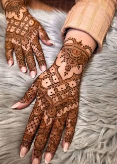 two hands with henna tattoos on them, one is showing off the intricate design