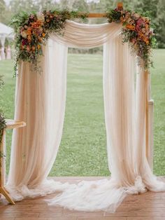 an outdoor wedding ceremony setup with sheer drapes and flowers on the back drop cloth