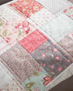 a patchwork quilt is laying on top of a tablecloth with pink and green flowers