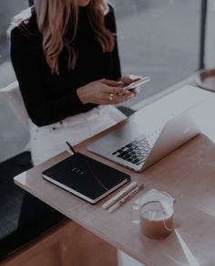 a woman sitting at a table looking at her cell phone and laptop with a glass of milk in front of her