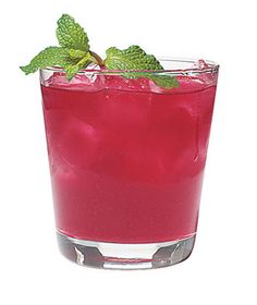 a red drink with mint on the rim in a clear glass next to a blue background