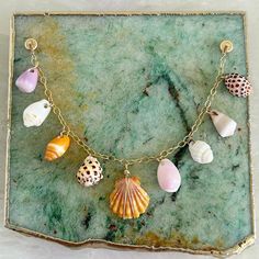 a sea shell necklace is displayed on a green marble slab with gold chains and seashells hanging from it