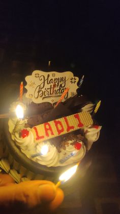 a birthday cake with candles on it in someone's hand and a sign that says happy birthday ladu