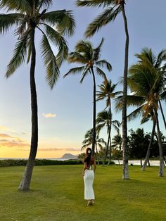 a woman in a white dress standing under palm trees