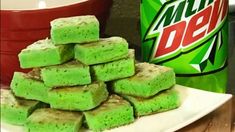 a pile of green squares sitting on top of a white plate next to a can of mountain dew