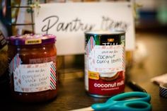 two jars of food sitting on top of a table next to scissors and a sign