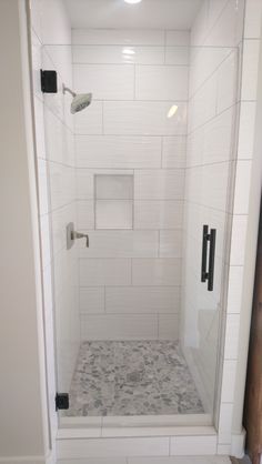 a walk in shower sitting next to a white tiled wall and floor with black handles