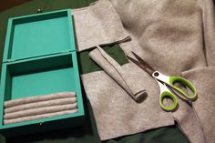 the scissors are laying on top of the sweaters in the box and next to it is another pair of scissors