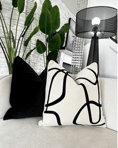 two black and white pillows sitting on top of a couch next to a green plant