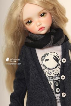 a doll with blonde hair wearing a gray shirt and black scarf over her shoulders,