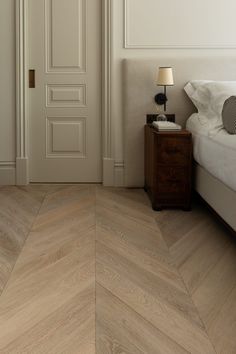 a bedroom with wood flooring and white walls, along with an open door to another room