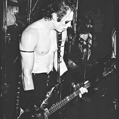 black and white photograph of a shirtless man playing bass in front of microphones