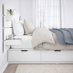 a bed with pillows and blankets on top of it next to a white shelf filled with books