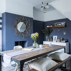 a dining room with blue walls and wooden table surrounded by white chairs, vases filled with yellow flowers