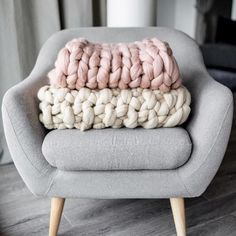 two knitted blankets sitting on top of a gray chair in front of a window