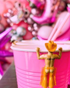 there is a toy man standing on top of a pink cup with plastic straws in it