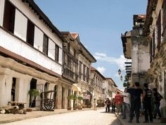 several people are walking down the street in front of some old buildings with balconies