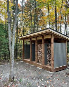 a small shed in the woods with lots of wood stacked up on top of it