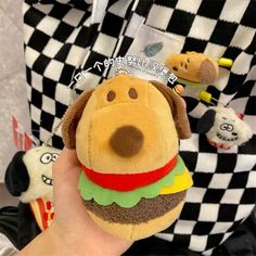 a hand holding a stuffed toy with a hamburger on it's face and other stuffed animals in the background