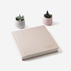 an open book sitting on top of a table next to two small potted plants