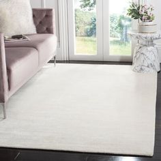 a living room area with a couch, chair and white rug on the hardwood floor