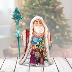 a santa clause figurine holding a blue staff on a table in front of a christmas tree