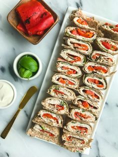 a platter filled with cut up sandwiches next to dipping sauces and green leaves