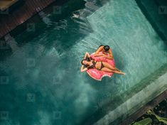 two women in pink swimsuits are floating on a surfboard near the edge of a pool