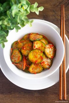 a white bowl filled with food next to chopsticks and a plant in the background