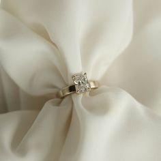 a diamond ring sitting on top of a white satin material covered in folds and fabric