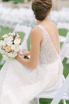 a woman in a wedding dress sitting on a white chair holding a bridal bouquet