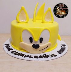 a yellow sonic cake with white frosting and black lettering on it's face