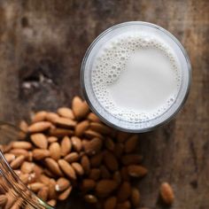 a glass filled with white liquid next to almonds on top of a wooden table