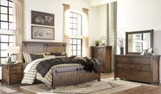 a bedroom with a bed, dresser and rug in front of two windows on the wall