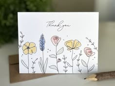 a thank you card with flowers on it and a pencil resting next to the card