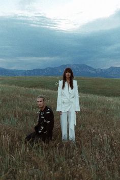 two people standing in a field with mountains in the background