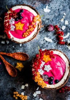 two desserts with berries and other toppings on a gray surface next to spoons