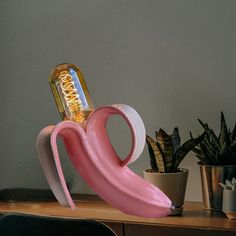 a pink flamingo shaped lamp sitting on top of a desk next to a potted plant