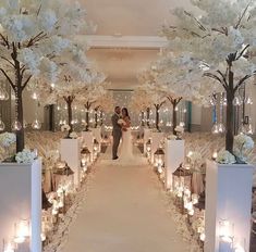 a bride and groom standing in front of an aisle decorated with flowers, candles and trees