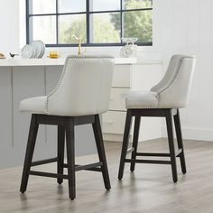 two white bar stools sitting next to each other in front of a kitchen counter