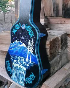 a guitar case painted with an image of mountains and trees in the night sky, sitting on top of a pile of wood