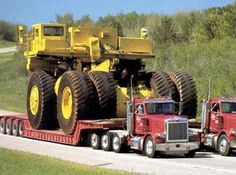 two large trucks on the back of a semi - truck driving down a country road