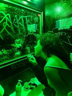 a woman writing on a blackboard in a dark room with green light from the window