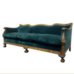 a green velvet couch sitting on top of a wooden frame with gold trimmings