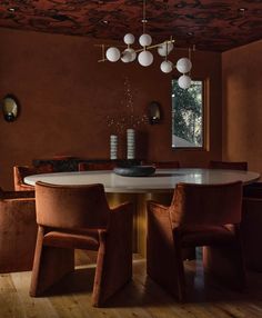 a dining room table with chairs and lights hanging from it's ceiling, in front of a window