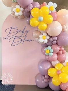 a baby in bloom sign with balloons and flowers on the front, along with a bouquet of daisies