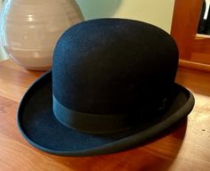 This is a vintage bowler hat (also known as a derby, coke hat, or bombín) crafted by Lamson Hubbard, a distinguished hat maker with roots in Boston and New York. Bowler hats have a rich history, originally designed by London hatters Thomas and William Bowler in 1849, and became iconic for their timeless style and sturdy construction. The hat is made of high-quality hard felt with a rounded crown and a classic silhouette, showcasing Lamson Hubbard's exceptional craftsmanship. The interior feature Vintage Brimmed Hat For Derby, Vintage Brimmed Derby Hat, Dark Blue Suit Men, Man Hats, Bob Hat, Mens Hats Vintage, Mens Vest Fashion, Dark Blue Suit, Blue Suit Men