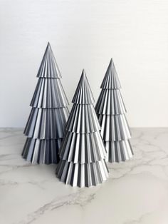 three metal christmas trees sitting on top of a marble countertop next to each other