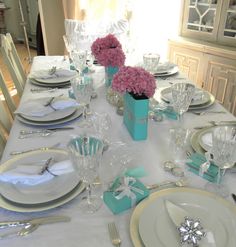 the table is set with white plates and silverware, pink flowers in vases