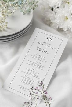 a table setting with white flowers and plates on the table, including a menu card